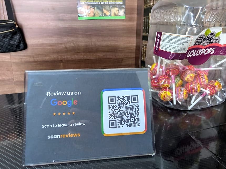 A ScanReviews Google review card on a barber shop counter beside a jar of lollipops