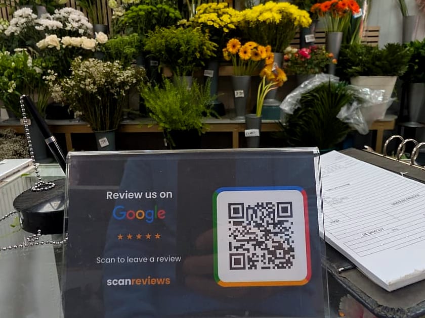 A ScanReviews Google review card on a florist counter with buckets of fresh flowers behind it